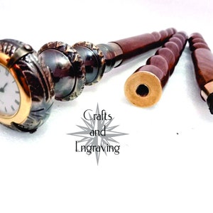May include: A walking stick with a brass clock face and a brown wooden handle. The stick is made of three sections that can be unscrewed and assembled. The clock face has Roman numerals and a gold-colored frame.