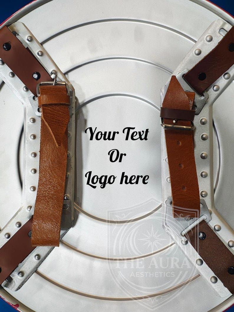 May include: A silver shield with brown leather straps and buckles. The shield has a circular design with rivets and the text "Your Text Or Logo here". The Aura Aesthetics logo is at the bottom.