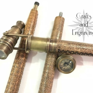 Op de afbeelding: Een wandelstok met een ingebouwde telescoop en kompas. De stok is gemaakt van hout en heeft een leren bekleding met een ingewikkeld patroon. De telescoop is van messing en heeft een zwarte lens. Het kompas is ook van messing en heeft een zwarte naald.