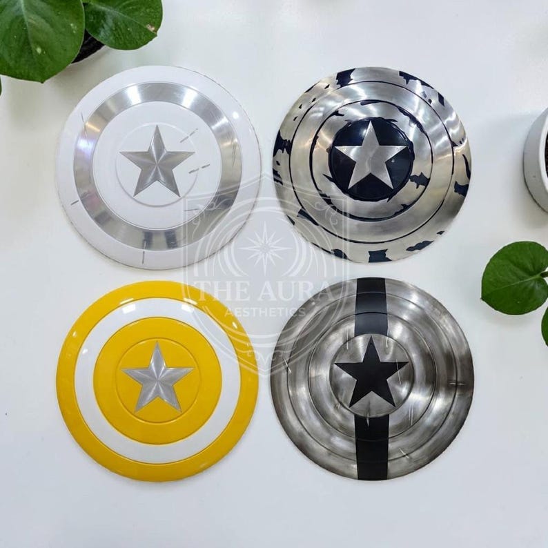 May include: Four circular shields featuring star designs. One is white and silver, another is distressed silver and black, a third is yellow and white, and the last is silver with a black stripe and star. The shields are likely themed after a superhero.