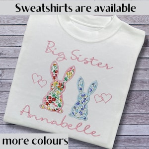 May include: White sweatshirt with pink embroidery that says "Big Sister Annabelle". The design includes two bunnies, one with pink and floral fabric and the other with blue and floral fabric.
