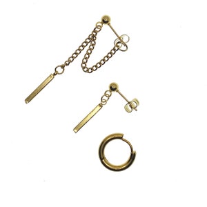 May include: Three gold-colored earrings on a white background. One pair features a chain connecting a stud to a dangling bar. Another earring has a stud with a dangling bar. The third earring is a small hoop.
