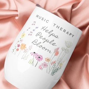 May include: White ceramic wine tumbler with a floral design and the text "Music Therapy Helps People Bloom".