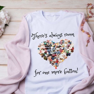 May include: White t-shirt with a heart-shaped design made of colorful buttons. The text "There's always room for one more button!" is printed below the heart.