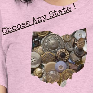 May include: A light pink t-shirt with the text "Choose Any State!" in black. The shirt features a graphic of the state of Ohio filled with various antique buttons in shades of gold, silver, and cream.