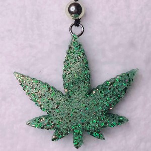 May include: A green glitter marijuana leaf charm with a silver bead and black cord.