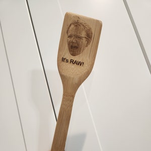 May include: A wooden spatula with a burnt-in image of a man's face and the text "It's RAW!"
