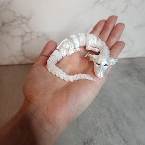 May include: A white, curled up, dragon figurine with black eyes. The dragon is made of a smooth, shiny material.