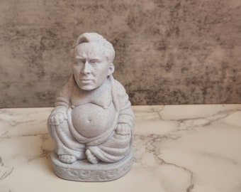 May include: A white ceramic figurine of a seated Buddha with a realistic face. The figurine has a speckled texture and is in a relaxed pose with hands resting on the lap.