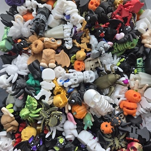 May include: A large collection of small, multi-colored plastic figurines featuring various Halloween-themed shapes including skulls, skeletons, bats, spiders, pumpkins, and various creatures in shades of white, orange, black, green, and purple.