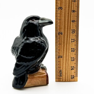 May include: A black ceramic raven figurine perched on a small wooden base. The raven is about 4 inches tall and has a detailed, realistic appearance.