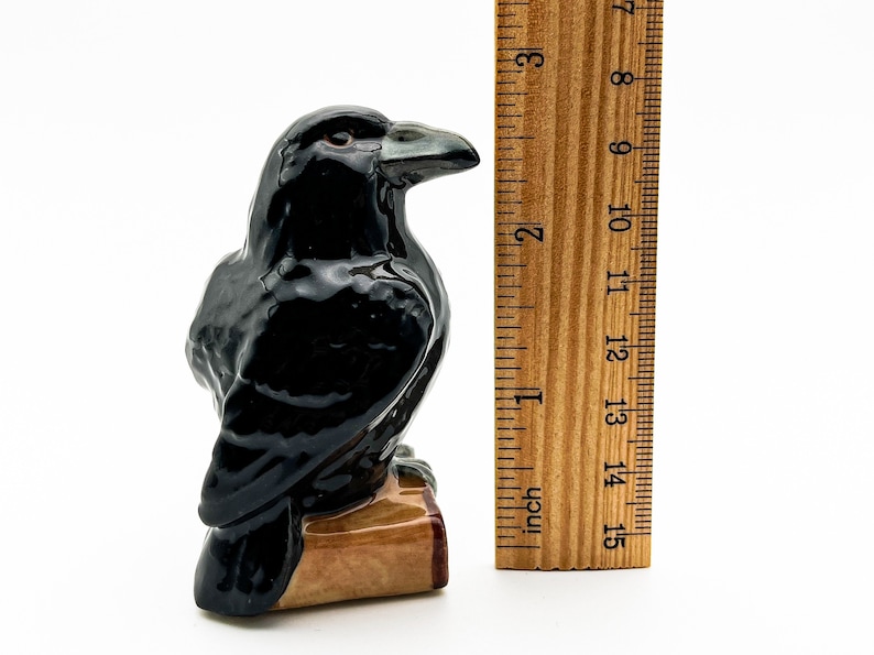 May include: A black ceramic raven figurine perched on a small wooden base. The raven is about 4 inches tall and has a detailed, realistic appearance.