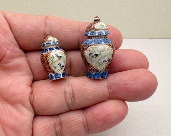 May include: Two miniature decorative ceramic vases with lids. The vases are brown, blue, and white, with a bird and foliage design. The vases are small, likely for display or decorative purposes.