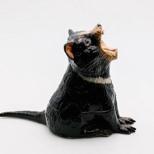 May include: A black and white ceramic figurine of a Tasmanian devil with its mouth open in a growl. The figurine is sitting on a white surface.