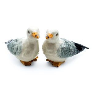Op de afbeelding: Twee keramische meeuwenbeeldjes, een naar links en een naar rechts gericht. Beide zijn wit met grijze en zwarte markeringen. Ze hebben oranje snavels en zwarte ogen.