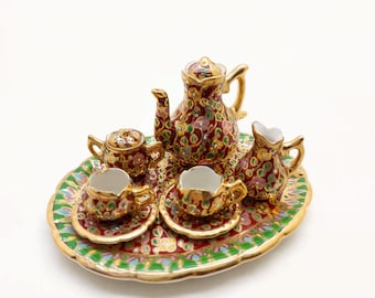 May include: A miniature porcelain tea set with a red, gold, and green floral design. The set includes a teapot, creamer, sugar bowl, and four cups and saucers. The set is on a matching tray.