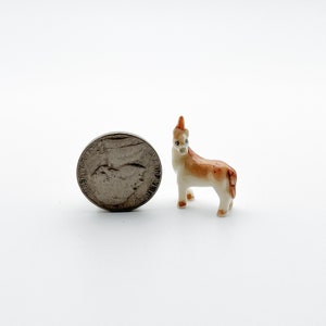 May include: A small, white porcelain figurine of a brown and white deer. The figurine is about the size of a US quarter.