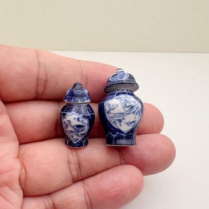 Peut inclure: Deux pots à gingembre en porcelaine bleu et blanc avec couvercle, l'un plus grand que l'autre, avec un motif floral. Les pots sont sur une main.