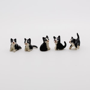 May include: Five miniature ceramic cat figurines. Each cat is black and white, with detailed facial features and varying poses. The cats are arranged on a white surface, showcasing their small size and intricate design.