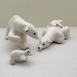 May include: A set of four white ceramic polar bear figurines. The figurines are in various poses, including a mother bear with a cub on her back, a standing bear, and a smaller cub.