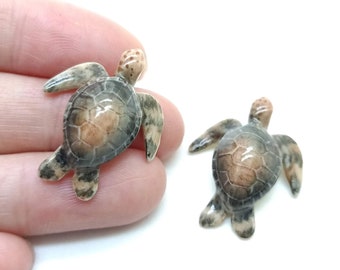 May include: Two small ceramic sea turtle figurines. The turtles are painted in shades of brown, gray, and white, with a realistic shell design.