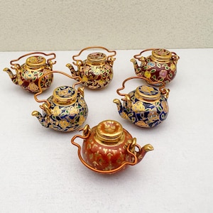 May include: A collection of six miniature decorative teapots. Each teapot features a detailed floral design in various colors, including red, blue, and gold. They have a small size and are adorned with a copper-colored handle.