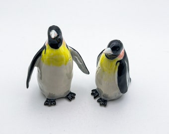 以下が含まれることがあります： セラミック製のペンギン型の塩コショウ入れ2個。左側のペンギンは前を向いて翼を広げている。右側のペンギンは左を向いて翼を閉じている。両方のペンギンは黒と白の模様と黄色のくちばしをしている。