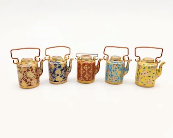 May include: Five miniature ceramic teapots with gold accents and floral patterns. The teapots are in shades of red, blue, yellow, and brown.