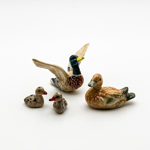 May include: A set of three ceramic duck figurines. The largest duck is a mallard with green and brown feathers. The other two ducks are smaller and brown with black spots.