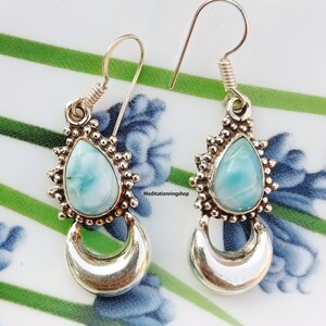 Könnte beinhalten: Ein Paar silberne Ohrhänger mit einem tropfenförmigen blauen und weißen Edelstein. Die Ohrringe haben ein Halbmond-Design am unteren Ende.