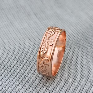 Pu&ograve; includere: Un anello in oro rosa con un motivo a foglie dettagliato. Il design dell'anello presenta foglie in rilievo e viticci a spirale, creando una superficie strutturata. L'anello &egrave; mostrato su uno sfondo neutro.