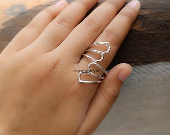 May include: A silver ring with a heart-shaped design. The ring features three connected heart shapes, creating a unique and stylish look. The ring is worn on a finger, showcasing its delicate and elegant design. The ring is made of a shiny, silver metal.