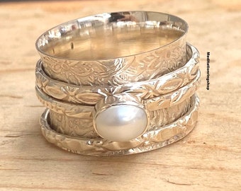 Könnte beinhalten: Ein silberner Drehring mit einer weißen Perle in der Mitte. Der Ring hat ein florales Design und besteht aus mehreren Bändern.