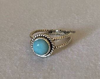 Può includere: Un anello d'argento con una fascia attorcigliata e una pietra preziosa blu chiaro incastonata in una montatura d'argento.