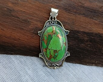 May include: Oval pendant with a vibrant green and copper-colored stone set in a silver-toned frame. The pendant has an ornate, detailed design with a bail at the top for a chain. The stone has a textured appearance.