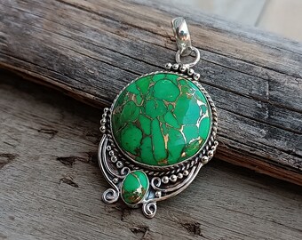 May include: A silver pendant with a green turquoise stone set in a circular design. The pendant has intricate silver detailing and a smaller green turquoise stone on the bottom.