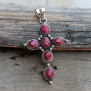 Könnte beinhalten: Ein silberner Kreuzanhänger mit sechs roten Rubin-Edelsteinen. Das Kreuz ist mit einem gedrehten Seil-Design und kleinen silbernen Perlen verziert.