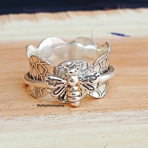May include: A silver ring with a bee design. The ring is made of a textured metal and has a honeycomb pattern. The bee is in the center of the ring and has a detailed design.