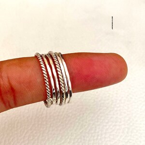 Könnte beinhalten: Ein Satz von fünf silbernen Stapelringen, jeder mit einer anderen Textur. Die Ringe werden an einem Finger getragen.
