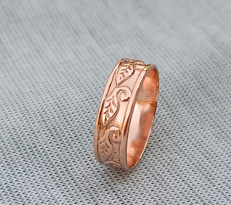 Pu&ograve; includere: Un anello in oro rosa con un motivo a foglie dettagliato. L'anello ha una larghezza della fascia di circa 0,64 cm. Le foglie e i viticci sono incisi nel metallo, creando una superficie strutturata. L'anello &egrave; esposto su una superficie grigio chiaro.