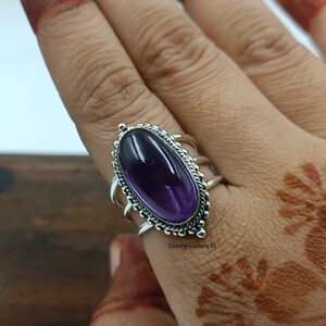 Könnte beinhalten: Ein silberner Ring mit einem ovalen, tiefvioletten Edelstein. Der Ring hat eine verzierte, detaillierte Fassung mit einem gewellten Rand und dekorativen Akzenten. Der Text "Silverjewellery30" ist sichtbar.
