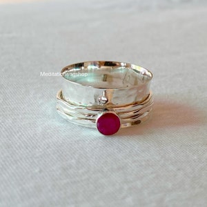 Könnte beinhalten: Ein silberner Drehring mit einem roten Edelstein. Der Ring ist gehämmert und hat eine strukturierte Oberfläche.