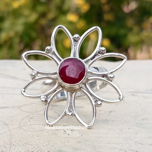 Puede incluir: Un anillo de plata con una piedra preciosa roja en el centro, con forma de flor de seis p&eacute;talos.