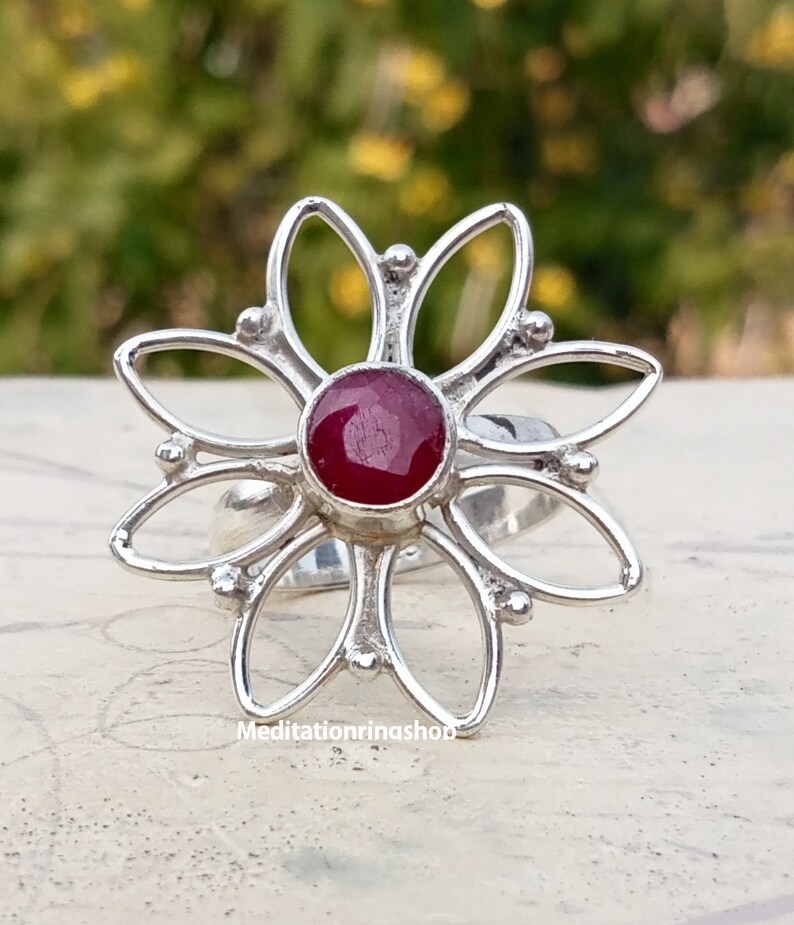 Puede incluir: Un anillo de plata con una piedra preciosa roja en el centro, con forma de flor de seis p&eacute;talos.