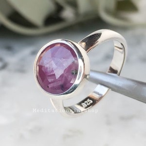 Könnte beinhalten: Ein silberner Ring mit einem runden, facettierten, violetten Edelstein. Der Ring ist mit "925" und "Meditationking Shop" gestempelt.