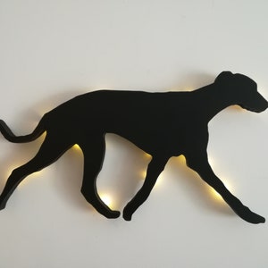 May include: Black silhouette of a dog running, cut out of wood and mounted on a white wall.