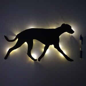 May include: A black silhouette of a dog running, lit up with small white lights. The silhouette is mounted on a white wall.
