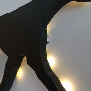 May include: Black silhouette of a dog with white lights outlining the shape. The lights are strung around the silhouette and are visible through the cut-out shape.