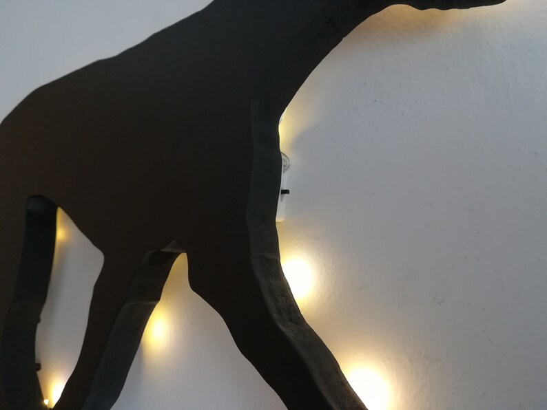 May include: Black silhouette of a dog with white lights outlining the shape. The lights are strung around the silhouette and are visible through the cut-out shape.