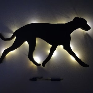 May include: A black silhouette of a dog running, lit up with white lights, mounted on a white wall.